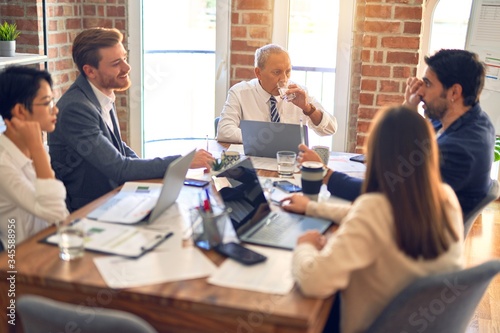 Group of business workers working together. Sitting on desk using laptop and talking at the office