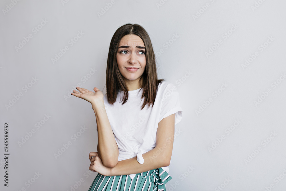 Lovable woman posing emotionally on light background. Worried caucasian girl with brown hair standing in studio. Lovable woman posing emotionally on light background. Worried caucasian girl with brown hair standing in studio.