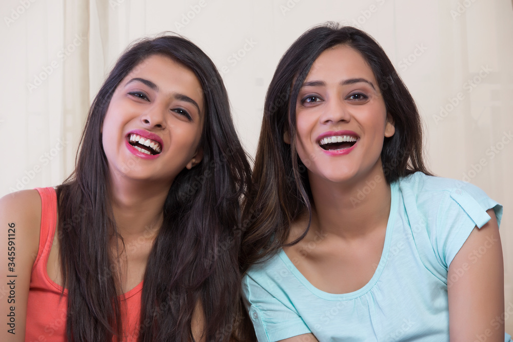 Two happy teenage girls sitting together at home and smiling
Two happy teenage girls sitting together at home and smiling