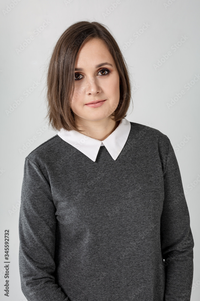 makeup brunette girl in a gray dress with a white collar on a white background. Light smile. Portrait. Vertical orientation. makeup brunette girl in a gray dress with a white collar on a white background. Light smile. Portrait. Vertical orientation.