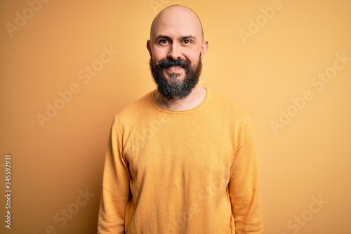 Handsome bald man with beard wearing casual sweater standing over yellow background with a happy and cool smile on face. Lucky person.