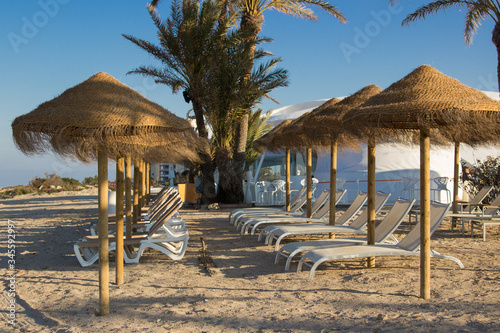 A row of sunbeds and sunshades in a deserted beach
