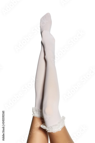 Cropped subject shot of lifted female legs in white shadow-proof stockings with ruffles on the top. The photo is made on the white background.  photo