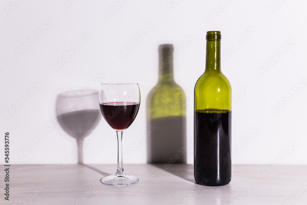 A glass of wine and a bottle casts a long shadow from the evening sun. A glass of wine and a bottle casts a long shadow from the evening sun.