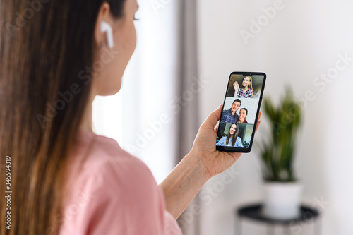 Video communication via smartphone. A young woman is using phone app for video call, online meeting. She talks with a several people together in same time. Close-up back view
