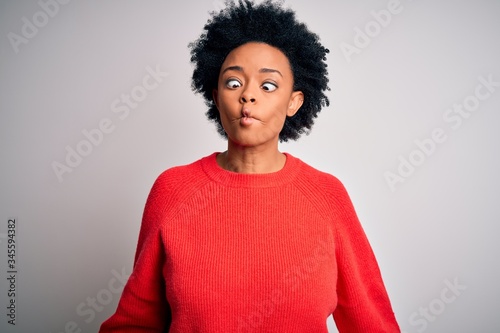 Young beautiful African American afro woman with curly hair wearing red casual sweater making fish face with lips, crazy and comical gesture. Funny expression.