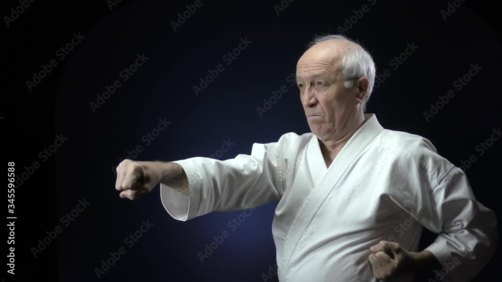 Against a dark blue background, an old athlete is training hand punches Against a dark blue background, an old athlete is training hand punches