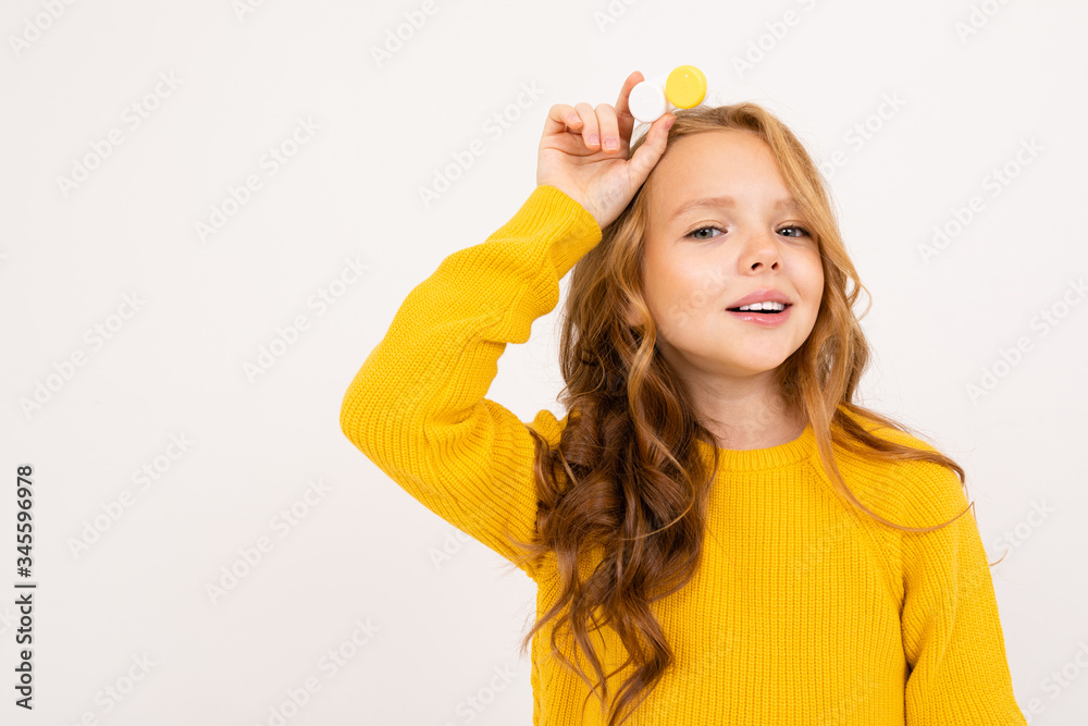 Happy teenager girl with red hair, hoody and yellow trousers holds contact lenses isolated on white background Happy teenager girl with red hair, hoody and yellow trousers holds contact lenses isolated on white background