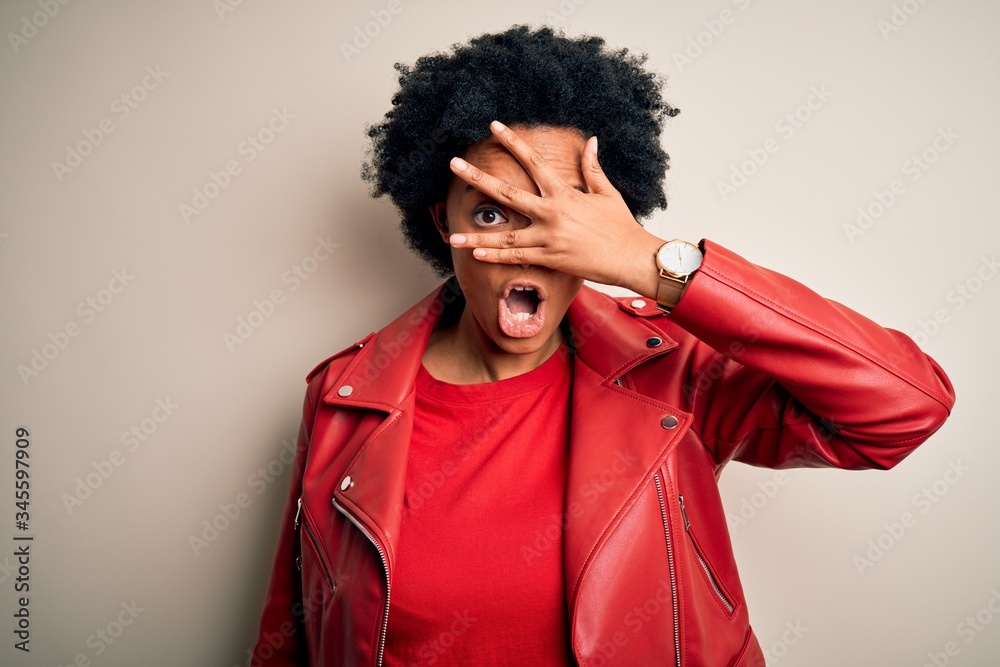 Young beautiful African American afro woman with curly hair wearing casual red jacket peeking in shock covering face and eyes with hand, looking through fingers with embarrassed expression. Young beautiful African American afro woman with curly hair wearing casual red jacket peeking in shock covering face and eyes with hand, looking through fingers with embarrassed expression.