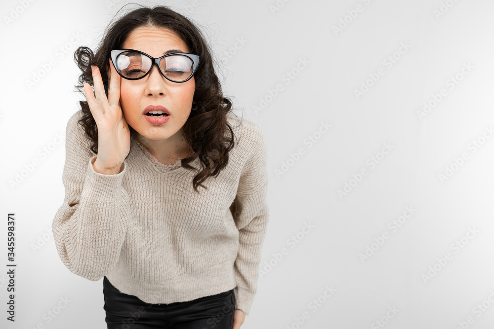 brunette woman squints holding glasses in her hand on gray background with copy space