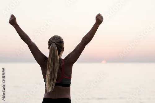 Young woman standing by the sea with arms raised in triumph