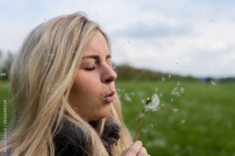Attractive blonde woman blows the seeds of a dandelion Attractive blonde woman blows the seeds of a dandelion