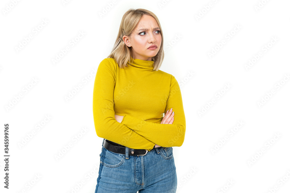close-up of a young woman with blonde hairstyle dressed in jeans and a yellow sweater with an indignant look on her face on a white isolated background close-up of a young woman with blonde hairstyle dressed in jeans and a yellow sweater with an indignant look on her face on a white isolated background
