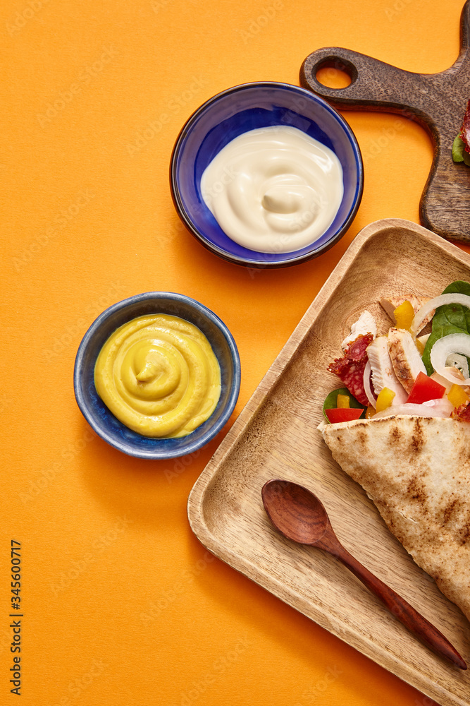 top view of fresh burrito with chicken and vegetables on board near chili sauce on orange background top view of fresh burrito with chicken and vegetables on board near chili sauce on orange background