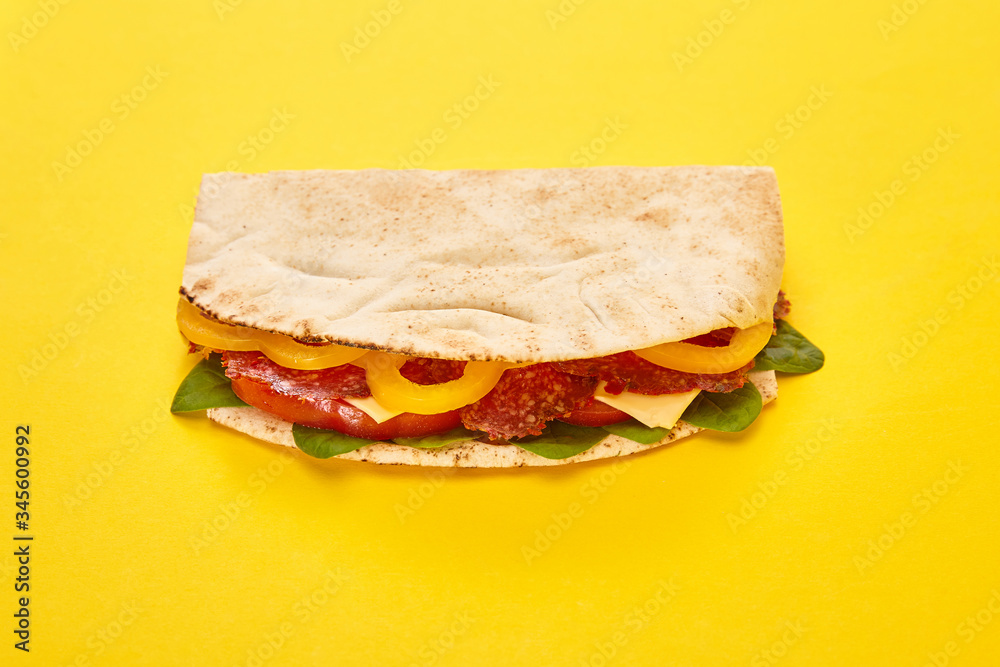 Obraz premium fresh sandwich with salami, pita, vegetables and cheese on yellow background