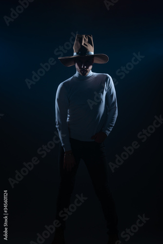 Portrait of a sexy young man with cowboy hat posing in a studio on high contrast and dark background