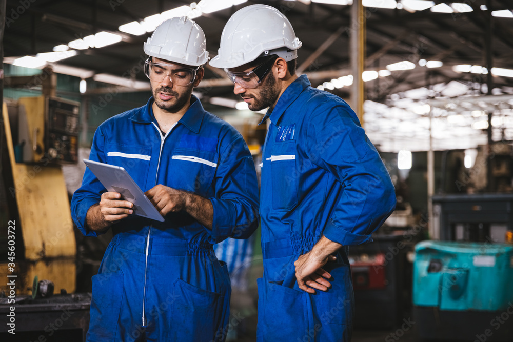 Industry maintenance engineer wearing uniform and safety helmet under inspection and checking production process on factory station by digital tablet. Industry, Engineer, construction concept.