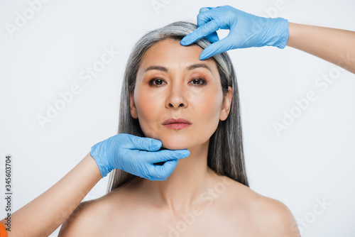 doctors in latex gloves touching face of naked asian woman with grey hair isolated on grey