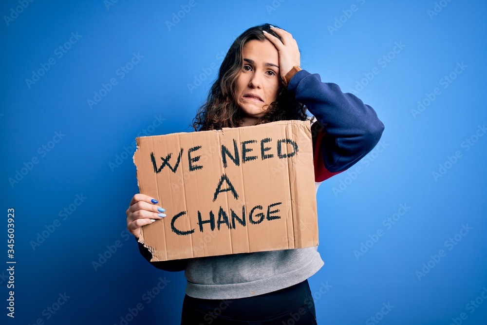 Young beautiful activist woman holding banner with change message over blue background stressed with hand on head, shocked with shame and surprise face, angry and frustrated. Fear and upset Young beautiful activist woman holding banner with change message over blue background stressed with hand on head, shocked with shame and surprise face, angry and frustrated. Fear and upset