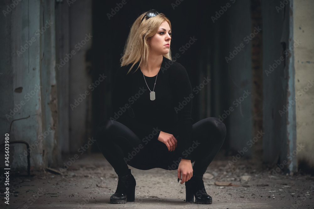A young woman is sitting among dark hall of abandoned building.