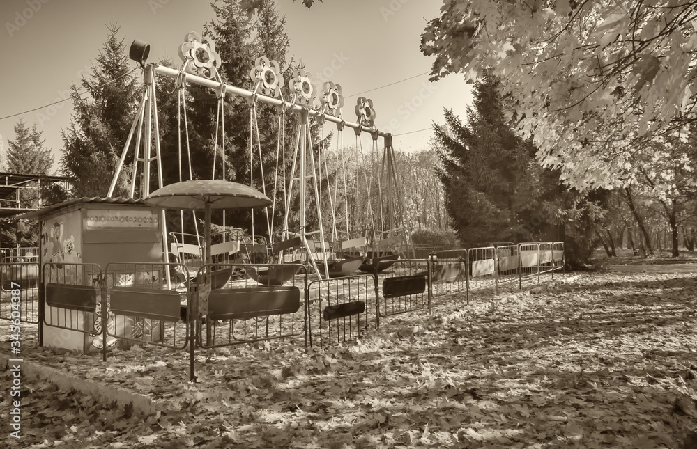 Fototapeta premium Kharkiv Park of Culture and Rest. Retro swing for children. Horizontal frame. Black and white photography, sepia. Photographed in Ukraine.