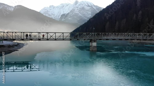 Circular pan by drone around bridge on blue lake with mountains in the background 
