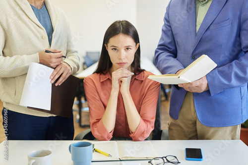 Angry young Caucasian woman sitting at office desk feeling stressed out at work, unrecognizable colleague and boss annoying her