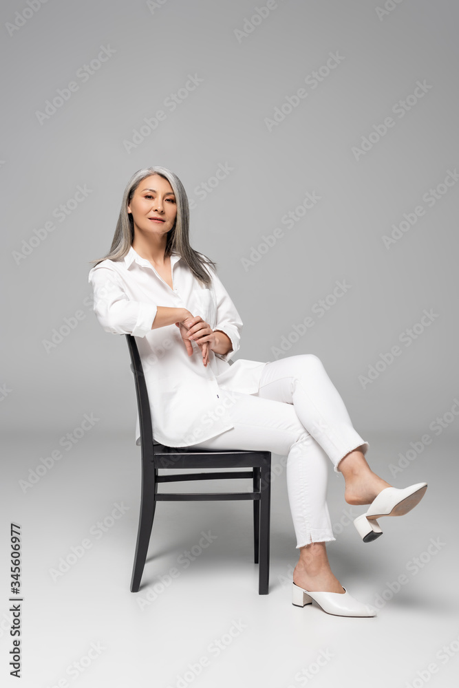 beautiful confident asian woman with grey hair sitting on chair on grey beautiful confident asian woman with grey hair sitting on chair on grey