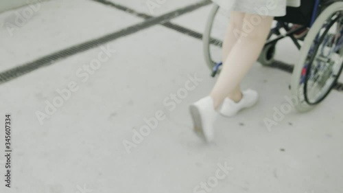 Woman is rolling invalid carriage with young man outdoors, close-up of legs photo