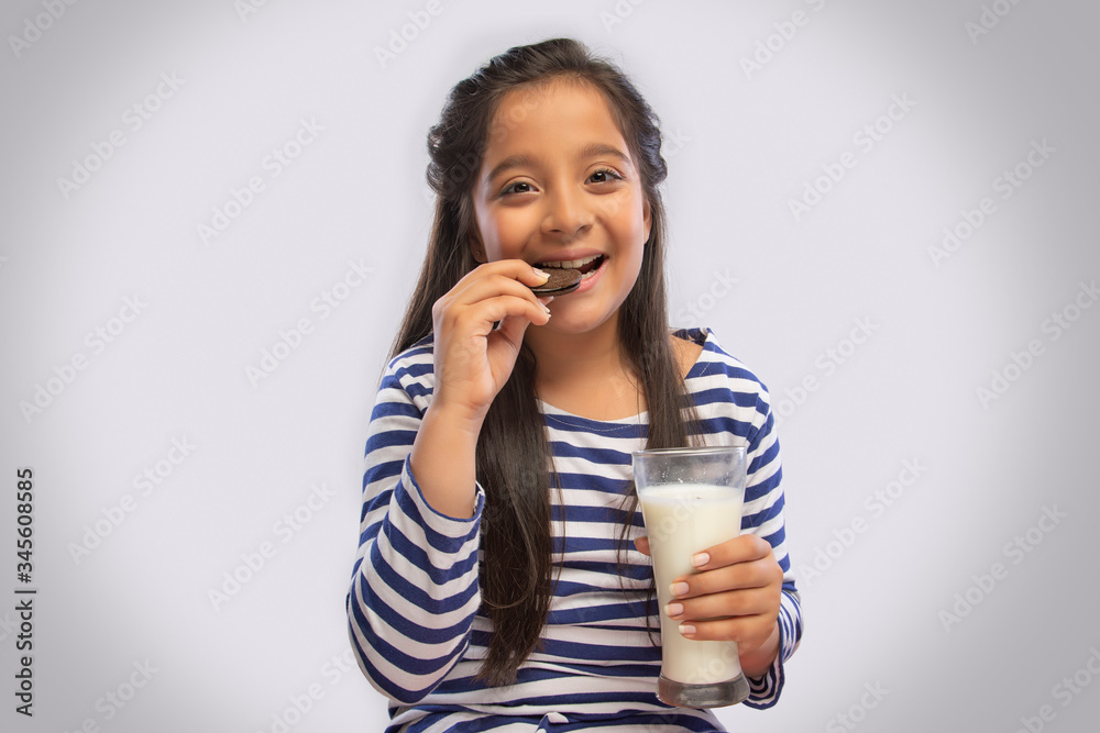 Smiling girl eating a cream biscuit while holding a glass of milk in one hand
Smiling girl eating a cream biscuit while holding a glass of milk in one hand