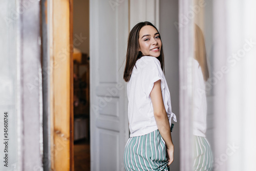 Inspired female model in white t-shirt relaxing in weekend morning. Indoor portrait of smiling caucasian lady wears trendy clothes at home. Free Download Inspired female model in white t-shirt relaxing in weekend morning. Indoor portrait of smiling caucasian lady wears trendy clothes at home. - GFXLoad
