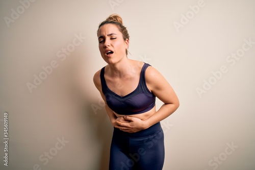 Young beautiful blonde sportswoman doing sport wearing sportswear over white background with hand on stomach because nausea, painful disease feeling unwell. Ache concept.