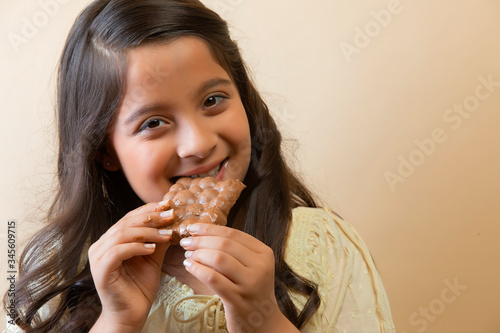 Smiling girl eating a chocolate bar with both hands 