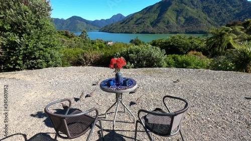 Outdoor table with a view on Pelorus Sound, Marlborough Sounds, South Island, New Zealand, Oceania.
Table with two chairs, two coffee mugs, and a vase with flowers. California quails running around th photo