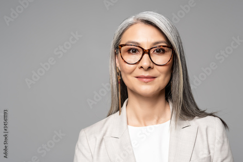 Obraz na plátně attractive smiling asian businesswoman in eyeglasses isolated on grey