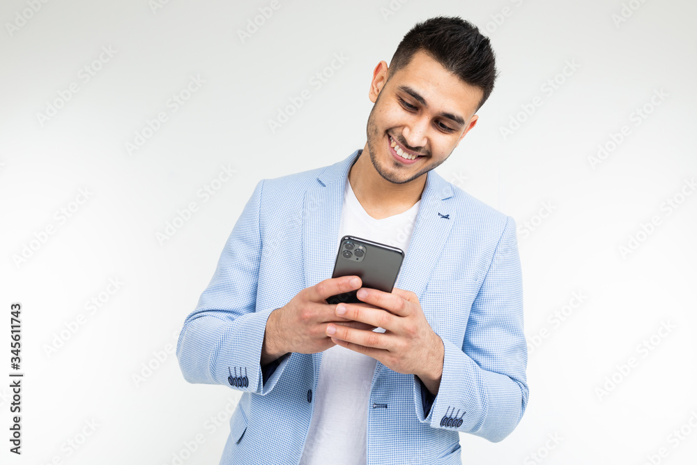 smiling stylish brunette man in a blue jacket looks at the phone on a white background smiling stylish brunette man in a blue jacket looks at the phone on a white background