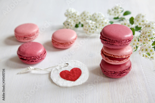 Pink macarons / macaroon on a white wooden table with tender white blossoms in the background and a gift tag with a heart.