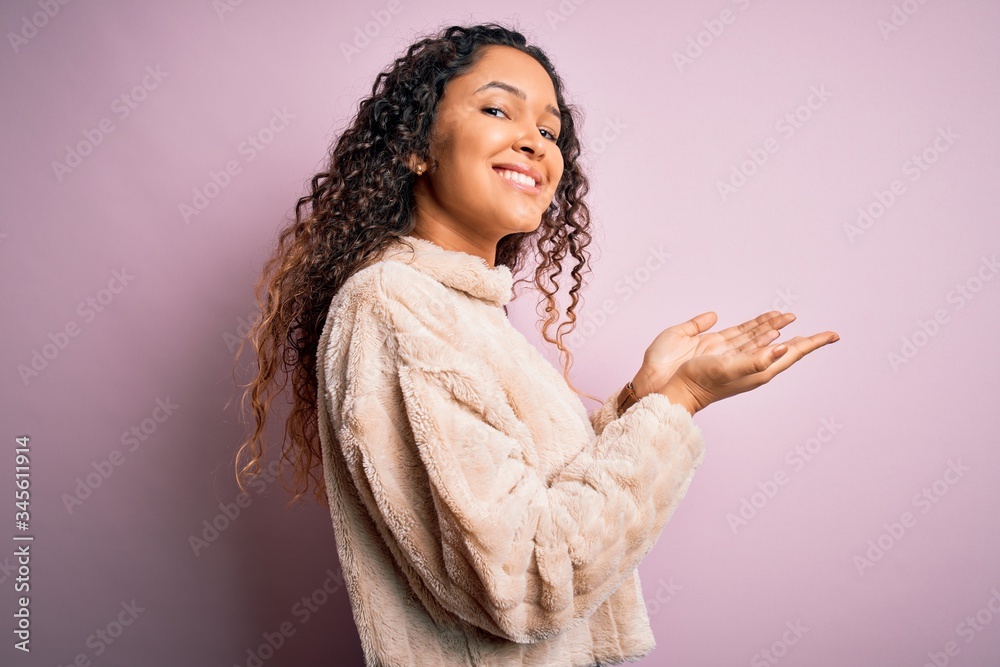 Young beautiful woman with curly hair wearing casual sweater standing over pink background pointing aside with hands open palms showing copy space, presenting advertisement smiling excited happy Young beautiful woman with curly hair wearing casual sweater standing over pink background pointing aside with hands open palms showing copy space, presenting advertisement smiling excited happy
