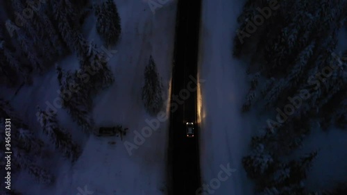 Aerial shot of car driving on curvy road in snowy landscape at night