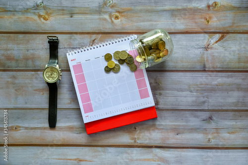 May calendar with hand watch and coins on wooden desk