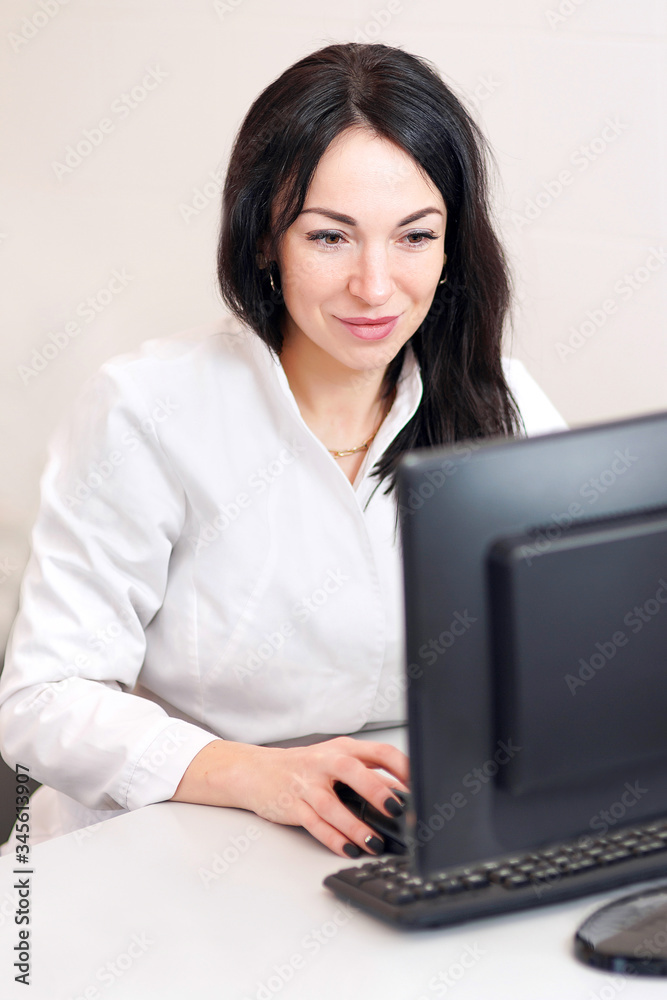 Searching for information. Dark-haired doctor in a white robe working on a computer. smiles Searching for information. Dark-haired doctor in a white robe working on a computer. smiles