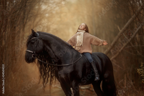 Little girl with Friesian stallion with long hair outdoor portrait in an autumn forest