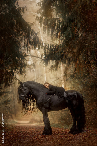 Little girl with Friesian stallion with long hair outdoor portrait in an autumn forest © Julia Shepeleva