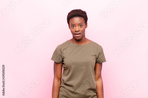 young pretty black womanlooking very shocked or surprised, staring with open mouth saying wow against pink wall photo