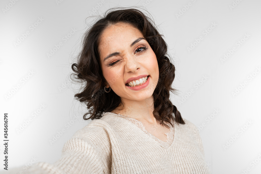 Beautiful brunette girl with makeup makes selfie while grimacing on gray studio background Beautiful brunette girl with makeup makes selfie while grimacing on gray studio background