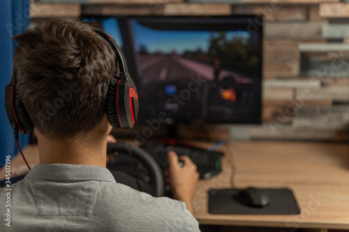 Entertainment concept, young man in headphones with pc computer playing car racing video game at home.