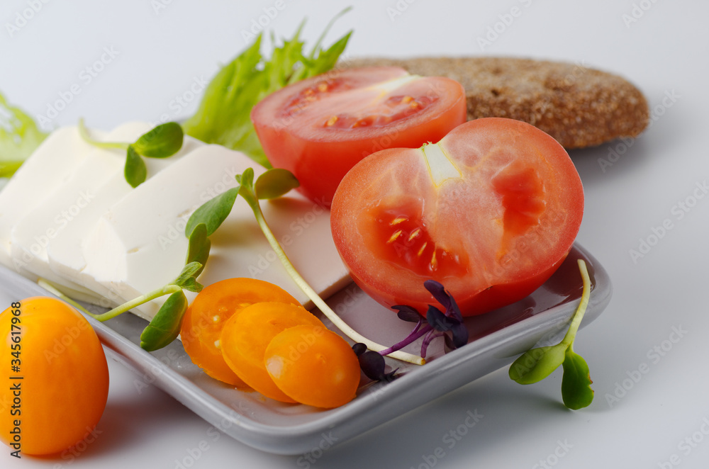 Sliced pink and yellow tomatoes and feta cheese on a plate with a piece of brown bread. Gray background. Selective focus. Sliced pink and yellow tomatoes and feta cheese on a plate with a piece of brown bread. Gray background. Selective focus.