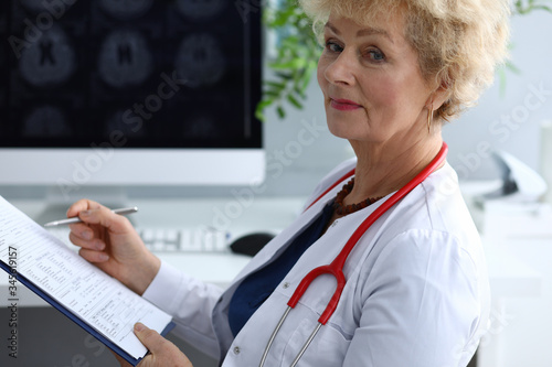 Portrait of professional senior doctor holding clipboard with prescription. Medical worker wearing uniform and red stethoscope. Modern medicine and qualified specialist concept