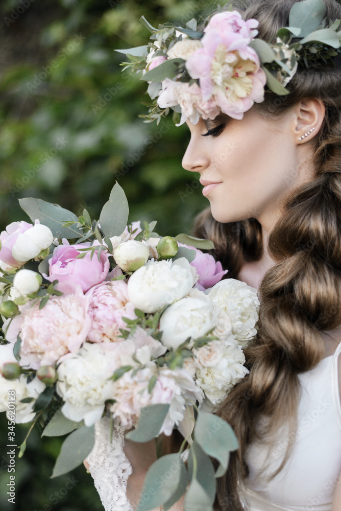 The bride holds a wedding bouquet, wedding dress, wedding details. wedding bouquet of peonies. Bride with snatural wreath of fresh flowers. Hairstyle from volumetric braids. lifestyle, fashion