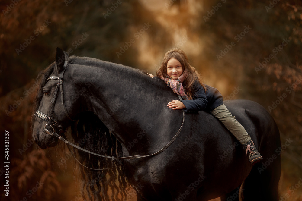 Obraz premium Little girl with Friesian stallion with long hair outdoor portrait in an autumn forest